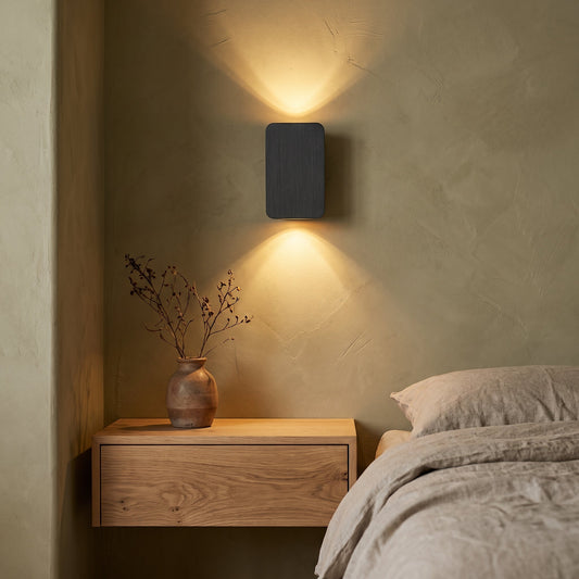 Charcoal Beam™ sconce washing warm light over an olive limewash bedroom wall above an oak nightstand