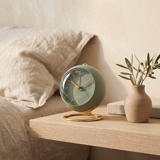 Globe alarm clock on an oak nightstand beside linen bedding