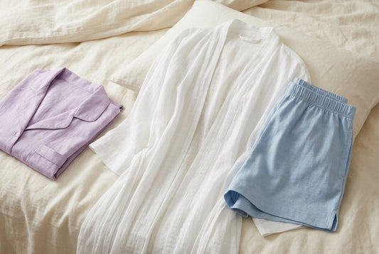 Lightweight pajama set, cotton robe and sleep shorts folded on linen bedding