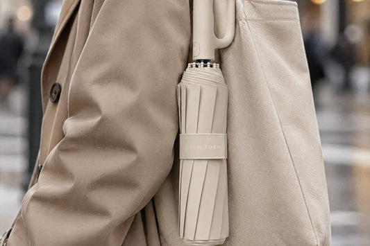 Folded beige Haven Umbrella clipped to the outside of a shoulder bag
