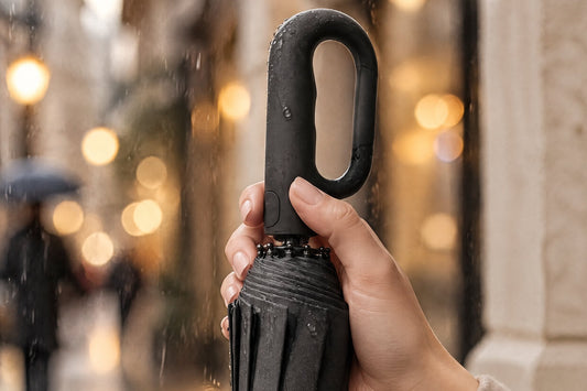 Hand holding a folded black Haven automatic umbrella by its carabiner handle in the rain