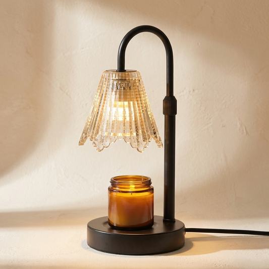 Taper candle warmer lamp with a black curved stem and ribbed glass shade shining down onto an amber jar candle