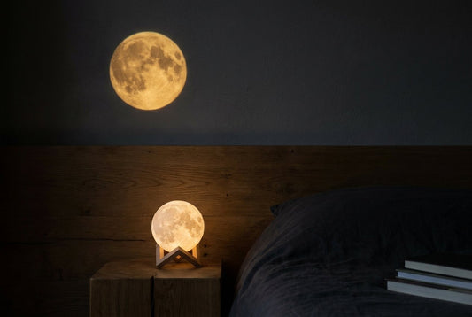 Projected golden moon on a bedroom wall beside a small glowing moon lamp