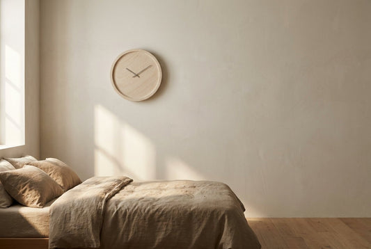 Pale round wall clock on a calm bedroom wall above linen bedding