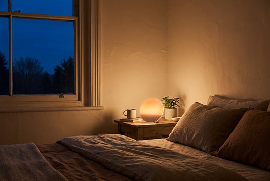 Sunrise wake-up light glowing warm orange on a bedside table before dawn