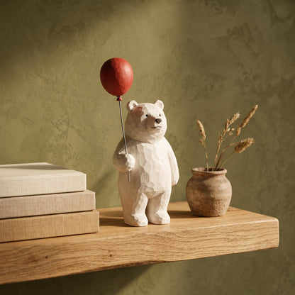 Bruin™ Carved Bear Ornament with red balloon on an oak shelf in Calm Eden style
