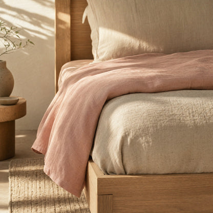 Blush linen sheet turned down over oatmeal duvet, bed corner detail