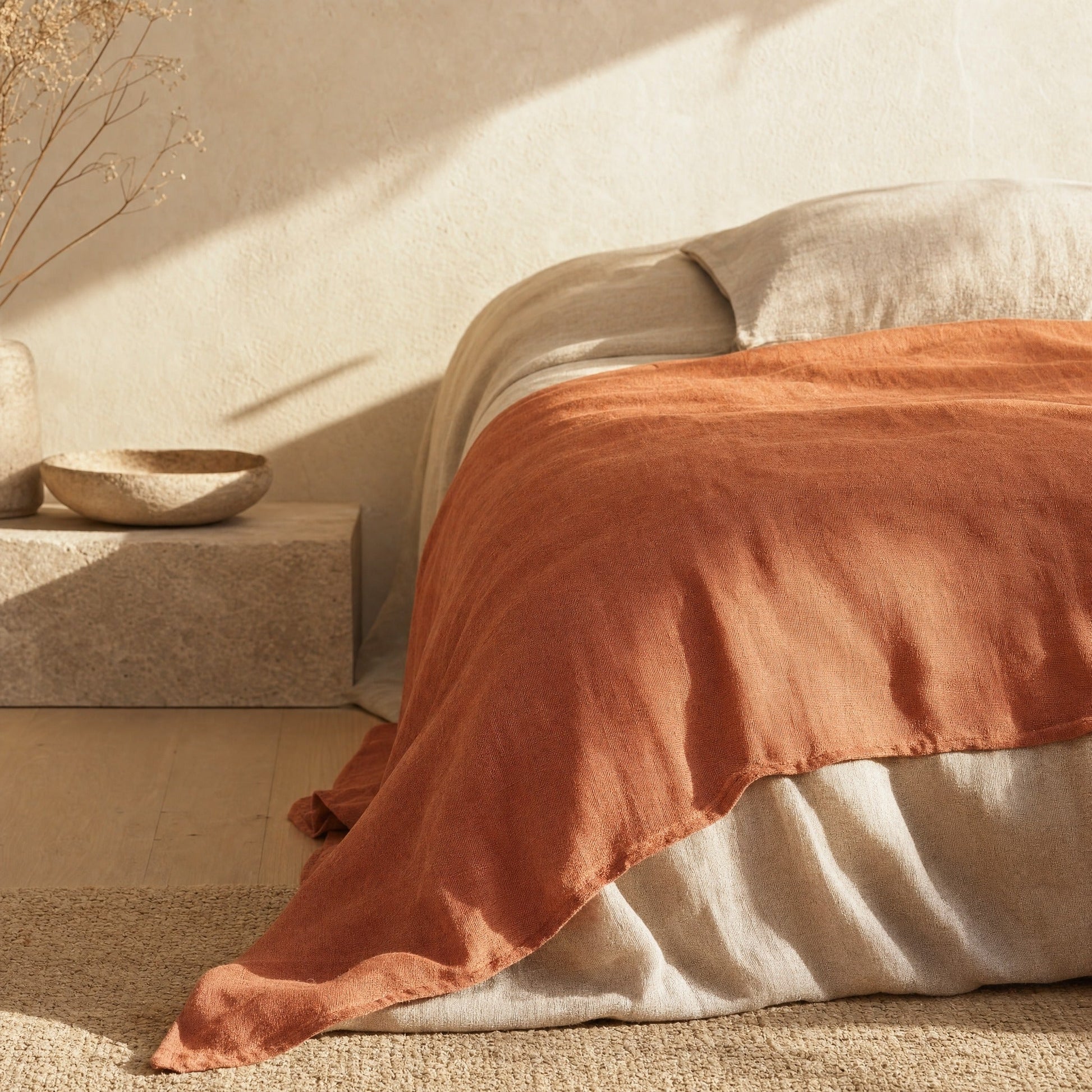 Clay linen sheet draped over bed corner in golden morning light