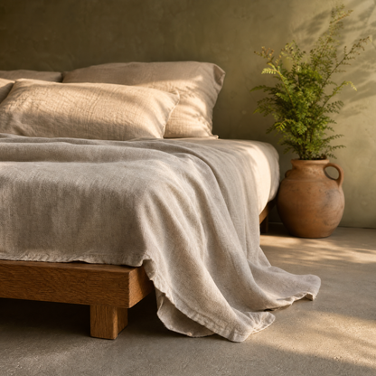 Flax oat linen sheet drape at the corner of an oak bed in golden light
