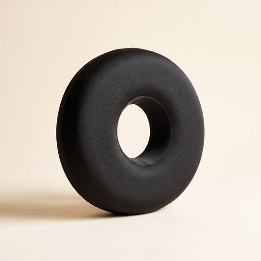 Ring™ Ear Relief Pillow — charcoal donut pillow with centre ear hole on warm cream background