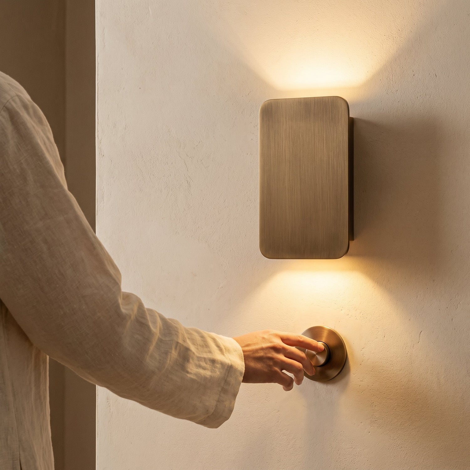 Hand on the dimmer beside a lit bronze Beam™ sconce at dusk