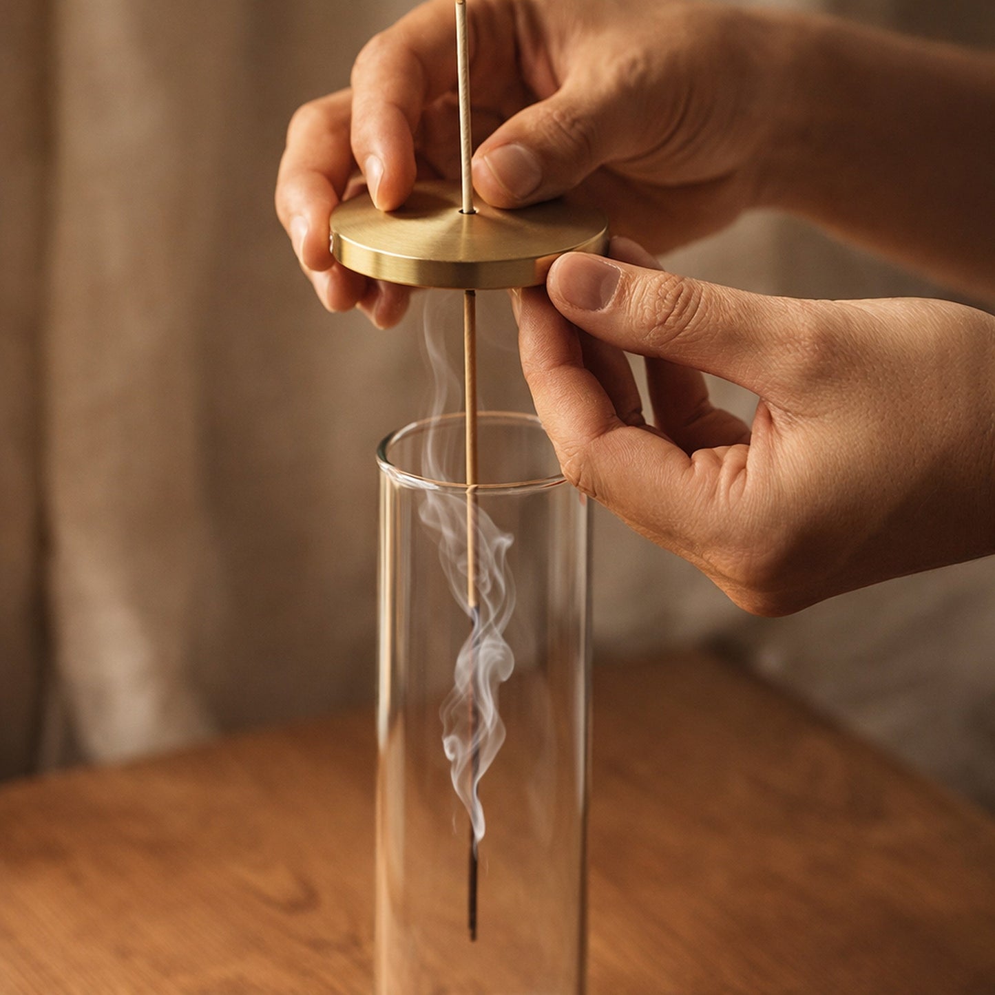 Hands lowering the threaded incense stick and brass lid into the glass tube