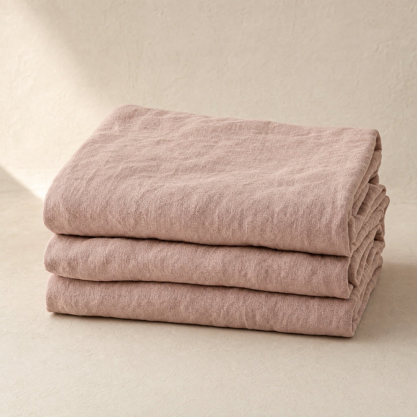 Flax blush French linen flat sheet folded stack on warm limewash plaster