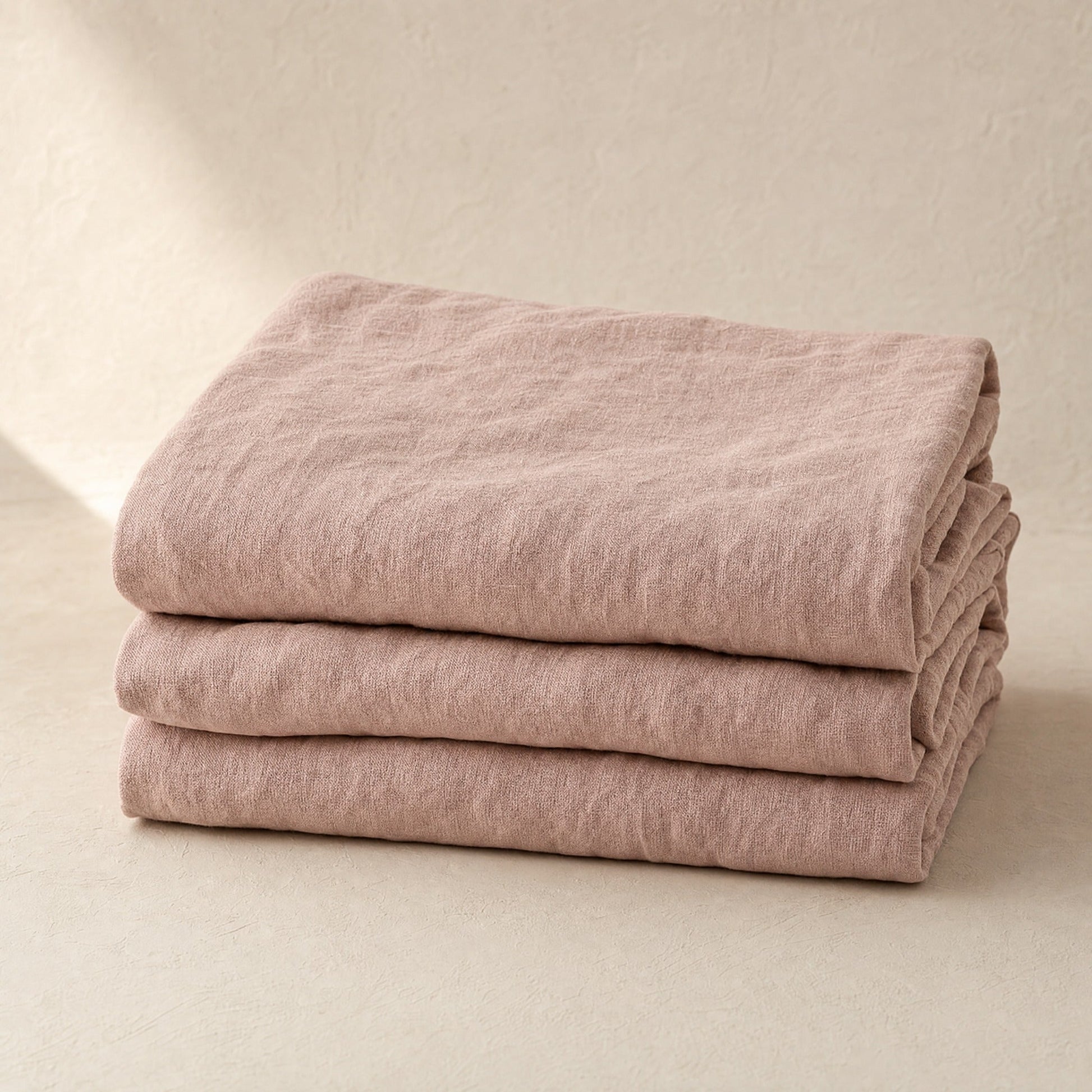 Flax blush French linen flat sheet folded stack on warm limewash plaster