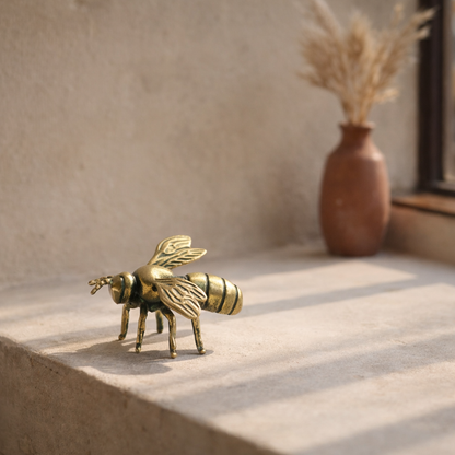 The brass bee standing on a pale limewashed windowsill beside a terracotta vase of dried grasses in late-morning sun