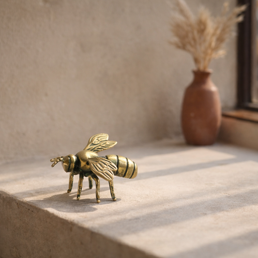 The brass bee standing on a pale limewashed windowsill beside a terracotta vase of dried grasses in late-morning sun