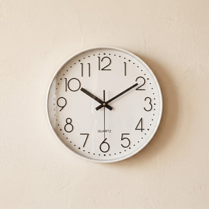 Hush Clock in All White hanging on a warm cream plaster wall