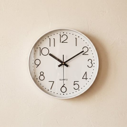 Hush Clock in All White hanging on a warm cream plaster wall
