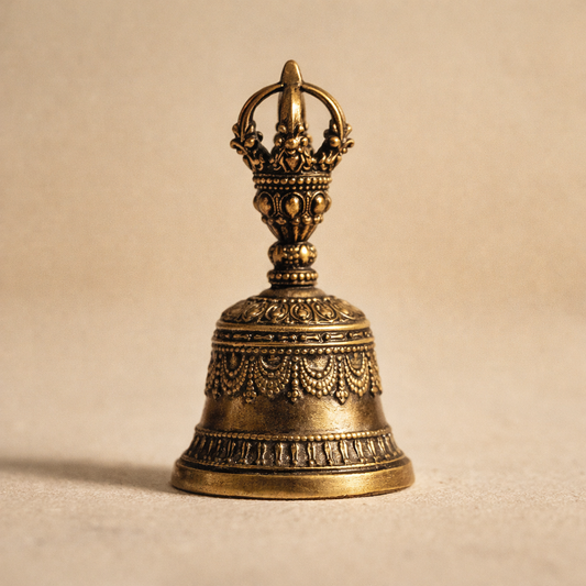 Drop™ Bronze Bell standing upright on warm cream plaster, a 5.2 cm die-cast solid bronze bell with beaded relief and a cast arched loop
