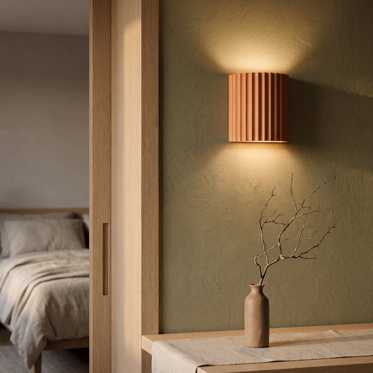 Terracotta Flute sconce washing warm light on an olive limewash wall beside an oak doorway