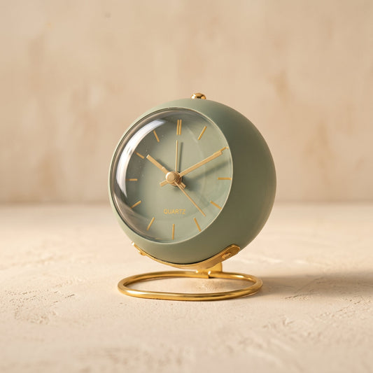 Globe alarm clock in sage green on a warm cream plaster surface
