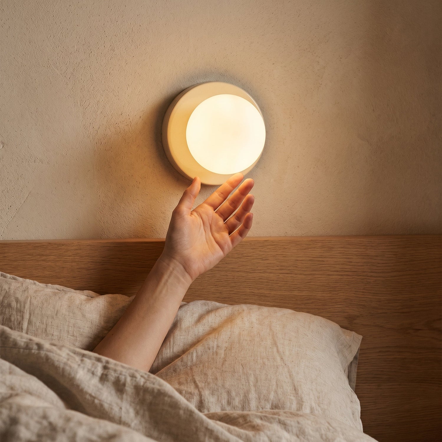 Hand reaching from bed toward the glowing Orb sconce above the oak headboard