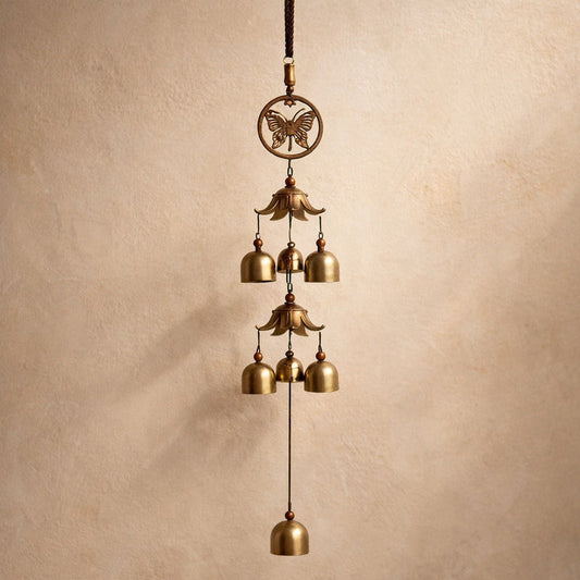 Peal Brass Bell Chime hanging against warm cream plaster, two tiers of small brass bells above a single weighted lower bell