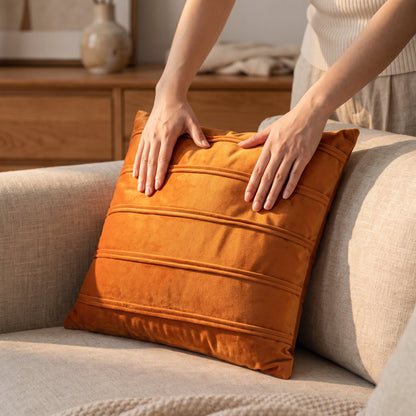 Hands plumping the amber Pleat velvet cushion on a linen sofa