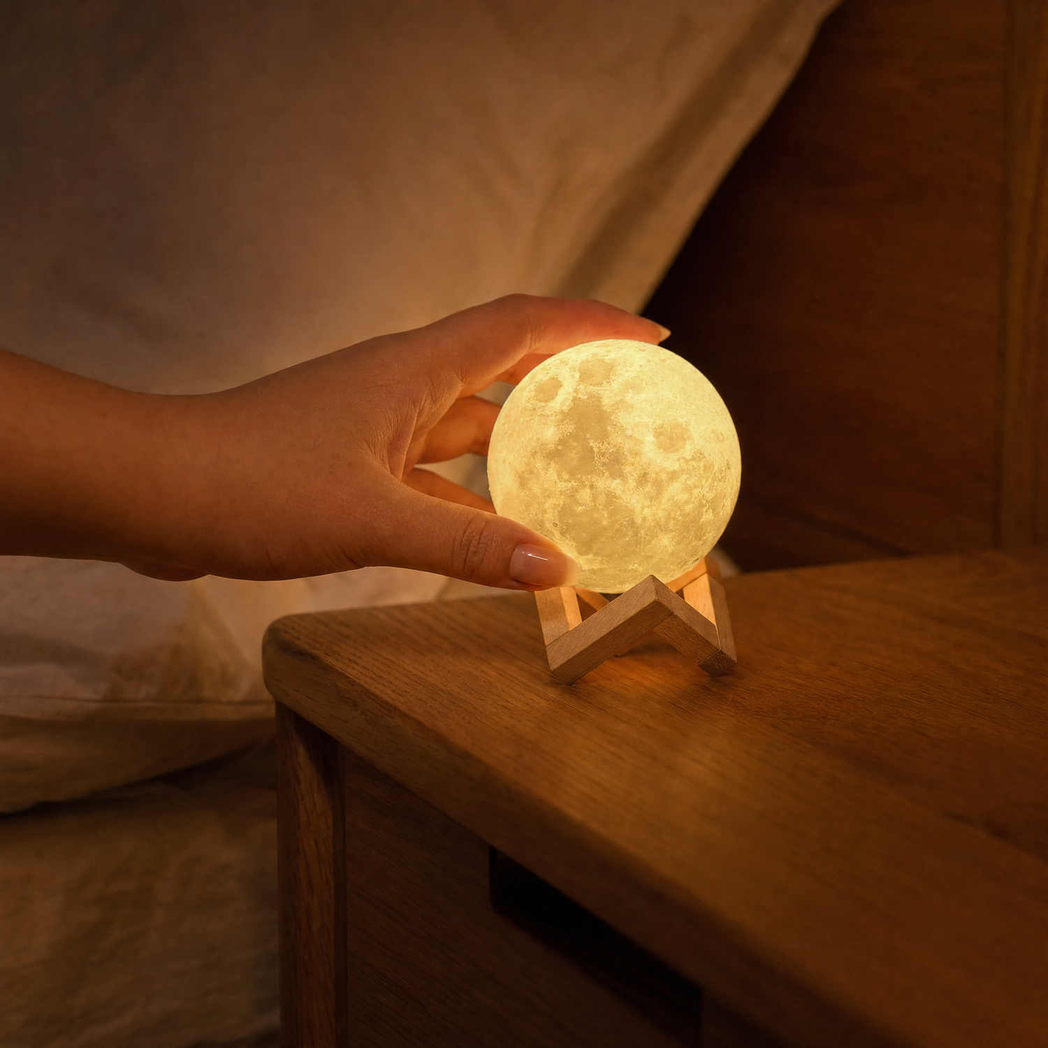 Hand placing the palm-sized Luna moon lamp onto its beech cradle at night