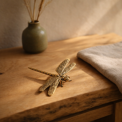 Brass dragonfly on an oak console beside an olive stoneware bud vase in warm afternoon light