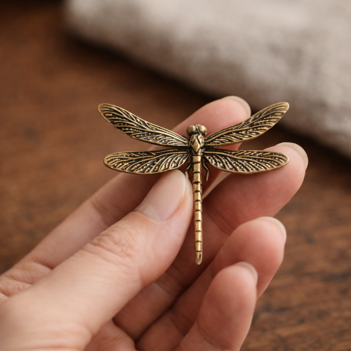 Brass dragonfly held between finger and thumb showing its 7.4 cm wingspan