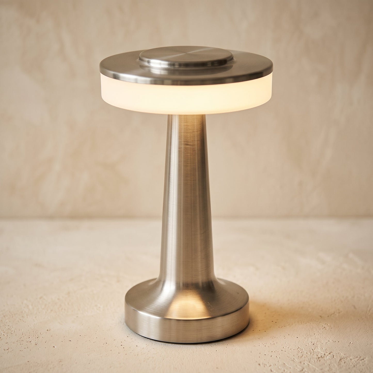 Stem cordless brushed nickel table lamp, lit warm on a cream plaster surface