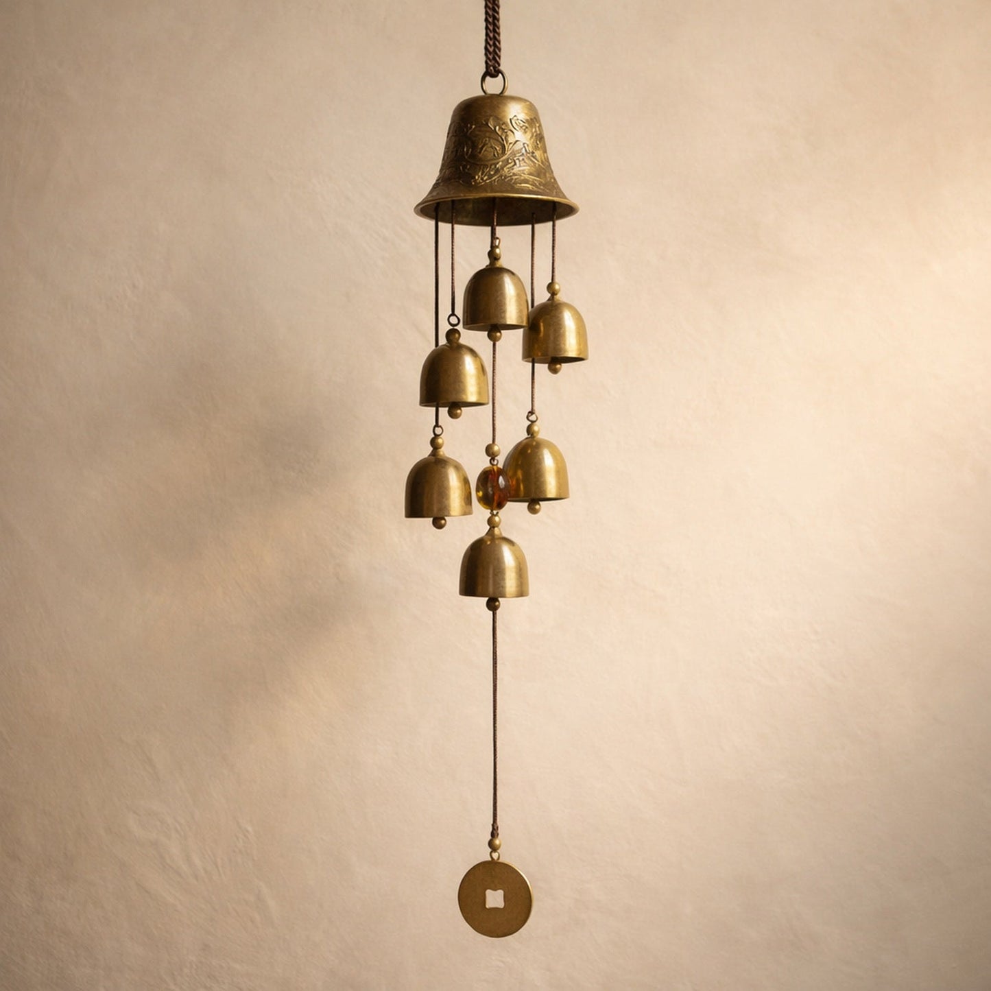 Toll™ Copper Wind Chime hanging against warm cream plaster — six small brass bells below an embossed crown bell