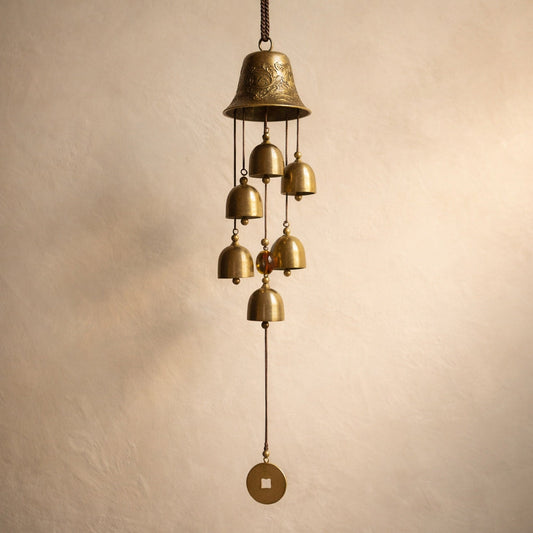 Toll™ Copper Wind Chime hanging against warm cream plaster — six small brass bells below an embossed crown bell