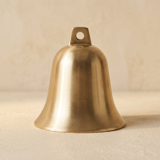 Vesper solid brushed brass bell standing upright on warm cream plaster