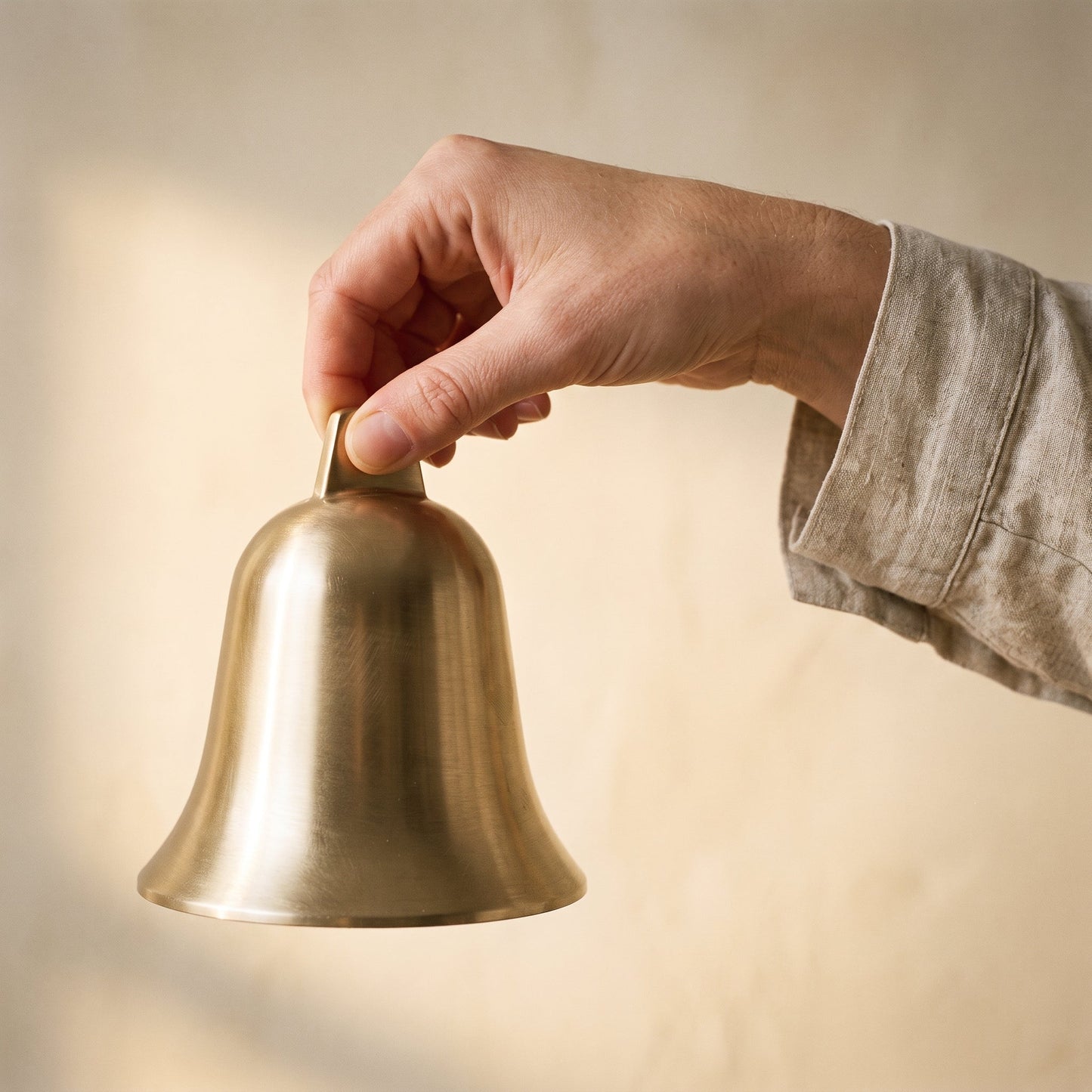 A hand lifting the Vesper brass bell by its pierced crown tab